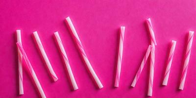 The primary subject of the image is a pink surface with a row of pink and white candy canes. The setting is a pink background, and the visual style is a close-up of the candy canes. The colors and mood of the image are predominantly pink, creating a warm and inviting atmosphere.