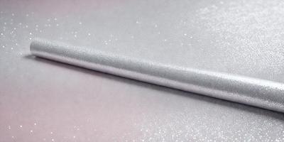 The primary subject of the image is a silver or grey fabric with a glittery texture. The setting is a table, and the visual style appears to be a photo. The colors in the image are predominantly silver and grey, creating a calm and sophisticated atmosphere.