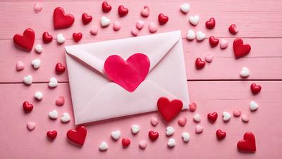 The primary subject of the image is a pink envelope with a heart-shaped stamp on it. The envelope is placed on a pink surface, which adds to the overall mood of the scene. The visual style of the image is a close-up of the envelope, showcasing its details and the heart-shaped stamp. The colors and mood of the image are predominantly pink, which gives it a warm and romantic atmosphere.