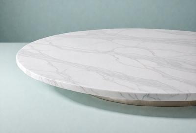 The primary subject of the image is a white marble tabletop. The table is round and has a smooth, polished surface. The setting is a blue background, which provides a contrasting and visually appealing backdrop for the table. The visual style of the image is a photo, capturing the details and texture of the marble tabletop. The colors and mood of the image are predominantly white and blue, creating a clean and elegant atmosphere.