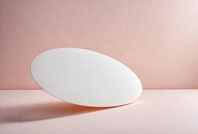 The primary subject of the image is a white, round, flat object, which appears to be a piece of paper or a small white plate. The setting is a pink surface, which adds a contrasting color to the scene. The visual style of the image is a close-up, focusing on the white object. The colors and mood of the image are predominantly pink, creating a warm and inviting atmosphere.