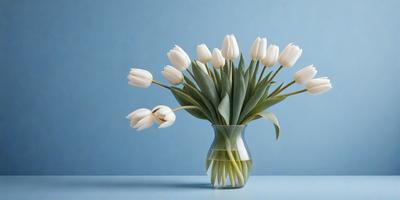 The primary subject of the image is a vase filled with white flowers, which are arranged in a bouquet. The vase is placed on a table, and the flowers are the main focus of the scene. The visual style of the image is a photo, capturing the beauty of the white flowers in a clear vase. The colors and mood of the image are predominantly white, creating a serene and peaceful atmosphere.