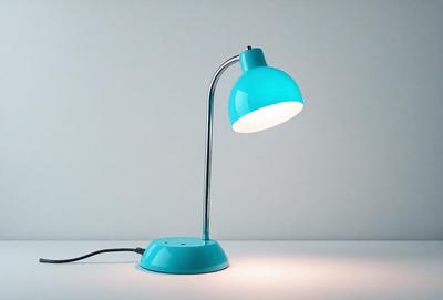 The primary subject of the image is a blue lamp with a white shade. The lamp is placed on a white table, which serves as the setting. The visual style of the image is a photo, capturing the lamp and its surroundings. The colors and mood of the image are predominantly white and blue, creating a clean and calming atmosphere.