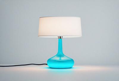 The primary subject of the image is a blue lamp with a white shade. The lamp is placed on a white table, which serves as the setting. The visual style of the image is a photo, capturing the lamp and its surroundings. The dominant colors in the image are blue and white, creating a calm and soothing atmosphere.