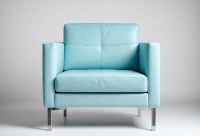The primary subject of the image is a blue leather chair. The chair is positioned in a white room, which serves as the setting and background. The visual style of the image is a photo, capturing the chair's details and colors. The dominant colors in the image are blue and white, creating a clean and modern atmosphere.