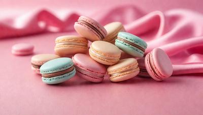 The primary subject of the image is a pink surface with a variety of macaroon cookies arranged on it. The cookies are in different colors and sizes, creating a visually appealing and appetizing display. The setting appears to be a kitchen or a dining area, as the cookies are placed on a table or counter. The visual style of the image is a close-up of the cookies, showcasing their details and textures. The colors and mood of the image are predominantly pink, which adds a