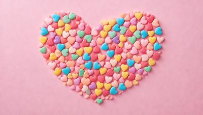 The primary subject of the image is a heart-shaped arrangement of various colored hearts. The hearts are placed on a pink background, creating a visually appealing and colorful display. The hearts come in different shapes and sizes, adding variety to the overall composition. The visual style of the image is a combination of photo and digital art, as it showcases a creative and artistic arrangement of hearts. The colors and mood of the image are predominantly pink, which adds a sense of warmth and love to the