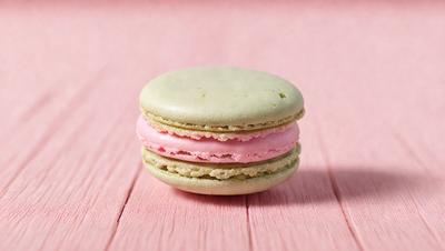 The primary subject of the image is a close-up of a macaroon sandwich, which is a delicious treat. The sandwich is made of two macaroons, one pink and one green, placed together. The setting is a pink surface, which adds a touch of color to the scene. The visual style of the image is a close-up, focusing on the details of the sandwich. The colors and mood of the image are vibrant and appetizing, making the sandwich look ent