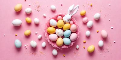 The primary subject of the image is a basket filled with colorful eggs. The basket is placed on a pink surface, which adds a vibrant and cheerful touch to the scene. The eggs come in various colors, including blue, pink, yellow, and white, creating a visually appealing and lively display. The overall atmosphere of the image is bright, cheerful, and inviting.
