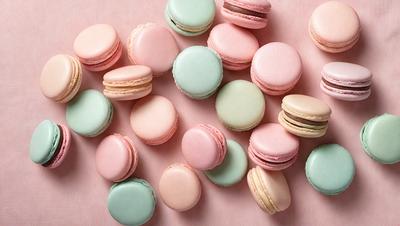 The primary subject of the image is a collection of macarons, which are small, round, and colorful pastries. They are arranged on a pink surface, creating a visually appealing display. The setting appears to be a kitchen or a bakery, as the macarons are presented in an organized manner. The visual style of the image is a close-up of the macarons, showcasing their vibrant colors and intricate designs. The overall atmosphere of the image is cheerful and inviting