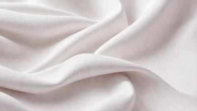 The primary subject of the image is a white sheet of fabric. The setting is a white background, which creates a clean and minimalist appearance. The visual style is a close-up of the fabric, showcasing its texture and details. The colors and mood of the image are predominantly white, giving it a calm and serene atmosphere.