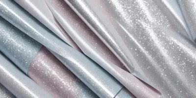 The primary subject of the image is a roll of silver and blue metallic paper. The paper is shiny and has a metallic texture. The setting is a table, and the visual style is a close-up of the paper. The dominant colors are silver and blue, creating a shiny and metallic appearance.
