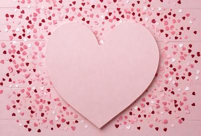 The primary subject of the image is a heart-shaped paper cutout. The heart is pink and is placed on a pink background. The visual style of the image is a combination of a photo and a digital art, as it appears to be a close-up of the heart with a patterned background. The colors and mood of the image are predominantly pink, creating a warm and romantic atmosphere.