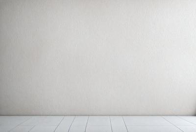The primary subject of the image is a white wall with a wooden floor. The setting is a room with a plain white wall, and the visual style is a photo. The colors and mood of the image are predominantly white, giving it a clean and minimalist appearance.