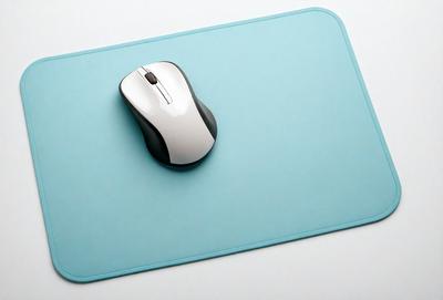 The primary subject of the image is a computer mouse. The mouse is placed on a blue mouse pad, which is sitting on a white surface. The visual style of the image is a photo, and the dominant colors are blue and white. The overall atmosphere of the image is clean and modern.