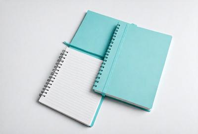 The primary subject of the image is a notebook and a notebook cover. The notebook is open and placed on a white surface. The notebook cover is blue and is placed on top of the open notebook. The setting is a white background, and the visual style is a photo. The colors and mood of the image are predominantly white and calm, with the blue notebook cover adding a touch of color and contrast.