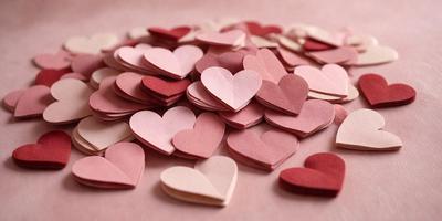 The primary subject of the image is a collection of pink and red heart-shaped stickers. These stickers are arranged on a pink surface, creating a visually appealing and playful scene. The setting appears to be a table or a similar surface, providing a suitable backdrop for the heart stickers. The visual style of the image is a close-up of the heart stickers, emphasizing their shape and color. The overall atmosphere of the image is cheerful and lighthearted, as the hearts evoke feelings