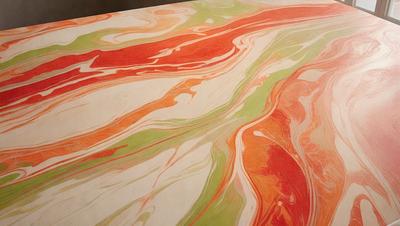 The primary subject of the image is a painting or drawing of a colorful, swirling pattern. The setting is a table or a surface where the artwork is displayed. The visual style appears to be a combination of digital art and illustration, with a vibrant and lively atmosphere. The colors used in the artwork are predominantly red, green, and orange, creating a striking and eye-catching pattern.