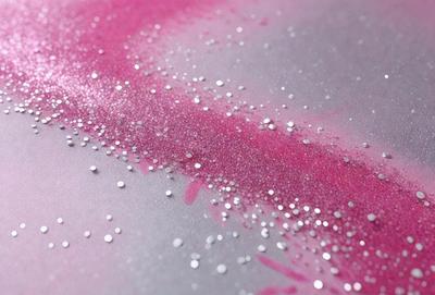 The primary subject of the image is a close-up of a pink and purple glittery surface. The setting is a gray background, which contrasts with the vibrant colors of the glitter. The visual style appears to be a combination of a photo and digital art, as the glittery surface is both realistic and artistic. The colors and mood of the image are lively and energetic, with the pink and purple hues creating a sense of warmth and excitement.