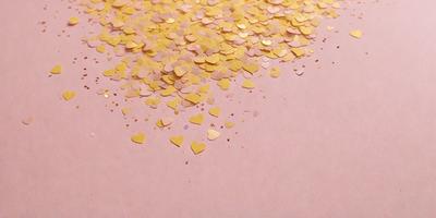 The primary subject of the image is a pink surface with gold hearts scattered across it. The setting is a pink background, and the visual style is a close-up of the hearts. The colors and mood of the image are warm and inviting, with the pink and gold creating a sense of love and affection.