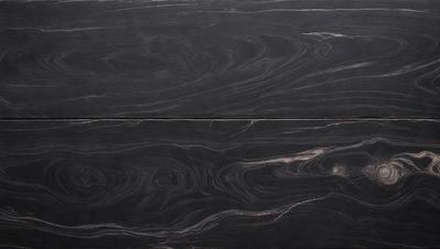 The primary subject of the image is a close-up of a wooden surface, possibly a table or a countertop. The setting is indoors, with the wooden surface being the main focus of the image. The visual style appears to be a close-up of a wooden surface, possibly a table or a countertop. The colors and mood of the image are predominantly dark, with the wooden surface being the main source of light and contrast.
