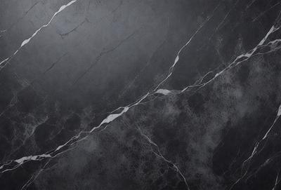 The primary subject of the image is a close-up of a marble surface, possibly a countertop or a wall. The setting is a dark room, which creates a moody atmosphere. The visual style is a black and white photo, giving the image a classic and timeless appearance. The colors and mood are predominantly dark, with the marble surface being the main focal point.