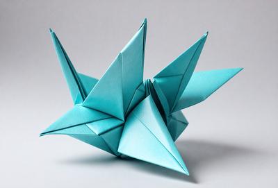 The primary subject of the image is a blue origami crane. The setting is a white background, and the visual style is a photo. The colors and mood of the image are predominantly blue, creating a calm and serene atmosphere.