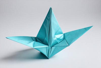 The primary subject of the image is a blue origami crane. The setting is a white background, and the visual style is a photo. The colors and mood of the image are predominantly blue, creating a calm and serene atmosphere.