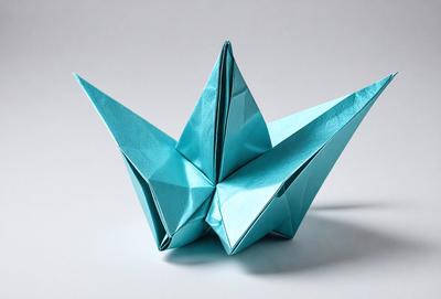 The primary subject of the image is a blue origami crane. The setting is a white background, and the visual style is a photo. The colors and mood of the image are predominantly blue, creating a calm and serene atmosphere.