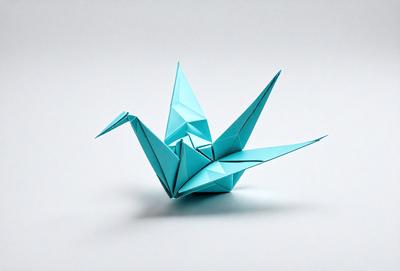 The primary subject of the image is a blue origami bird. The bird is sitting on a white surface, which serves as the background. The visual style of the image is a photo, capturing the intricate details of the origami bird. The colors and mood of the image are predominantly blue and calm, as the bird is the main focus and the white surface provides a clean and serene backdrop.