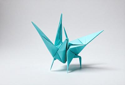 The primary subject of the image is a blue paper crane, which is a traditional Japanese art form. The crane is sitting on a white surface, which serves as the setting or background. The visual style of the image is a combination of photo and digital art, as it appears to be a close-up of the paper crane. The colors and mood of the image are predominantly blue and calm, as the crane is the main focus and the white surface provides a clean and serene backdrop.
