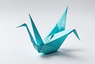 The primary subject of the image is a blue paper crane, which is a traditional Japanese art form. The crane is sitting on a white surface, which serves as the setting or background. The visual style of the image is a close-up of the paper crane, showcasing its intricate details. The colors and mood of the image are predominantly blue and calm, as the crane is a symbol of peace and tranquility.