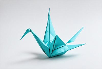 The primary subject of the image is a blue origami bird, which is the main focus of the scene. The bird is sitting on a white surface, which serves as the background. The visual style of the image is a photo, capturing the intricate details of the origami bird. The colors in the image are predominantly blue and white, creating a calm and serene atmosphere.