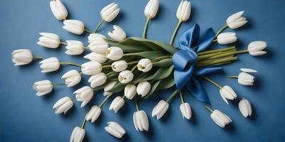 The primary subject of the image is a bouquet of white tulips. The setting is a blue background, which adds a contrasting and vibrant touch to the scene. The visual style is a close-up of the flowers, showcasing their details and beauty. The colors and mood of the image are predominantly white and blue, creating a serene and elegant atmosphere.