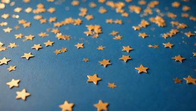 The primary subject of the image is a blue surface with a pattern of gold stars scattered across it. The setting appears to be a table or a similar surface, providing a backdrop for the stars. The visual style of the image is a combination of photo and digital art, creating a unique and eye-catching pattern. The dominant colors in the image are blue and gold, giving it a calm and serene atmosphere.