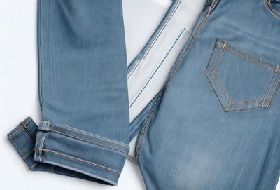 The primary subject of the image is a pair of blue jeans. The jeans are displayed on a white surface, which serves as the background. The visual style of the image is a close-up of the jeans, showcasing their details and texture. The colors in the image are predominantly blue, with the jeans being the main focus. The overall atmosphere of the image is casual and relaxed, as it features a common and familiar item of clothing.