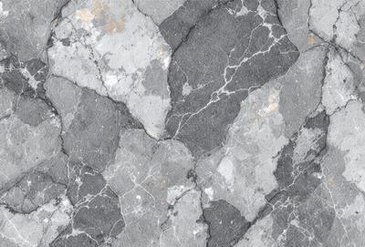 The primary subject of the image is a close-up of a marble surface with a pattern of holes and grooves. The setting is a stone wall, and the visual style is a photo. The dominant colors are gray and black, creating a moody atmosphere.