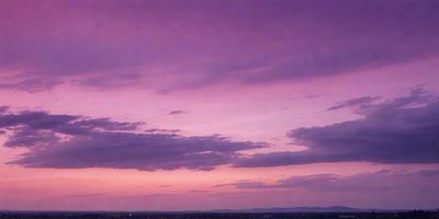 The primary subject of the image is a beautiful sunset with a purple sky. The setting is a cityscape with buildings and a mountain range in the background. The visual style is a photo, capturing the vibrant colors and the serene atmosphere of the sunset. The colors and mood of the image are predominantly purple, creating a sense of calmness and tranquility.