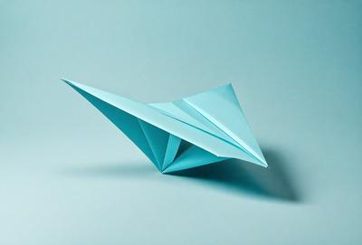 The primary subject of the image is a blue paper airplane. The setting is a blue background, which creates a contrasting and visually appealing scene. The visual style is a combination of photo and digital art, as the paper airplane appears to be a digital creation. The colors and mood of the image are predominantly blue, giving it a calm and serene atmosphere.