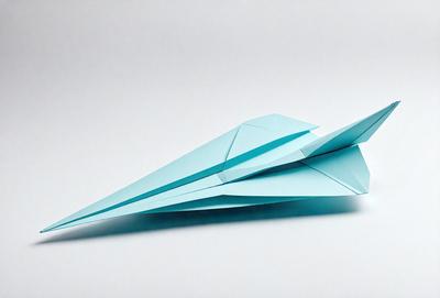 The primary subject of the image is a blue paper airplane. The setting is a white surface, which provides a clean and uncluttered backdrop for the airplane. The visual style is a simple, hand-drawn illustration of the paper airplane. The colors and mood of the image are predominantly blue, giving it a calm and soothing atmosphere.