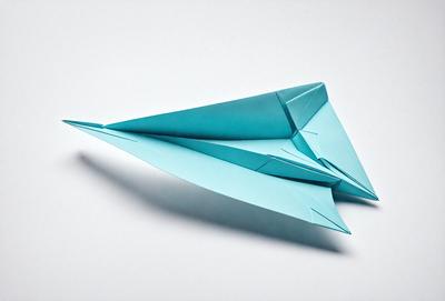 The primary subject of the image is a blue paper airplane. The setting is a white background, and the visual style is a photo. The colors and mood of the image are predominantly blue, creating a calm and serene atmosphere.