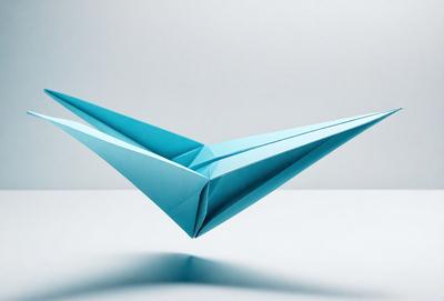 The primary subject of the image is a blue paper kite. The kite is sitting on a white surface, which serves as the setting or background. The visual style of the image is a photo, capturing the kite in its natural environment. The colors and mood of the image are predominantly blue, creating a calm and serene atmosphere.