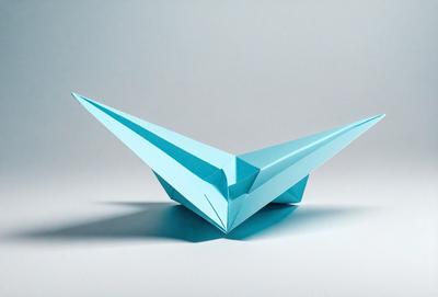 The primary subject of the image is a blue paper kite. The kite is sitting on a white surface, which serves as the background. The visual style of the image is a photo, capturing the details of the kite. The colors and mood of the image are predominantly blue, creating a calm and serene atmosphere.