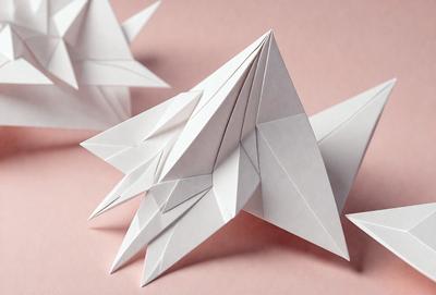 The primary subject of the image is a white paper star. The setting is a pink surface, which provides a contrasting background. The visual style is a close-up of the paper star, showcasing its details. The colors and mood of the image are predominantly white and pink, creating a warm and inviting atmosphere.