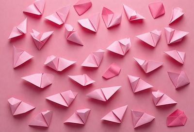 The primary subject of the image is a large number of pink paper airplanes. They are arranged in various positions and orientations, creating a visually interesting and colorful scene. The setting is a pink background, which adds to the overall mood and visual style of the image. The colors and mood of the image are predominantly pink, creating a warm and inviting atmosphere.