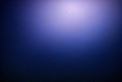 The primary subject of the image is a bright light in the sky, which appears to be a star. The setting is a dark, starry night with a blue background. The visual style is a photo, capturing the night sky with the star as the main focus. The colors and mood of the image are predominantly dark and moody, with the star being the only bright spot in the sky.