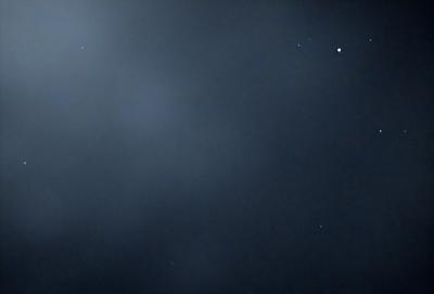 The primary subject of the image is the night sky, which is filled with stars. The setting is a dark, cloudy night, with the sky being the main focus of the image. The visual style is a photo, capturing the beauty of the night sky. The colors and mood of the image are predominantly dark and moody, with the stars being the main source of light in the scene.
