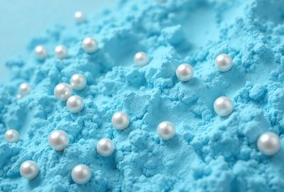 The primary subject of the image is a blue surface with numerous white pearls scattered across it. The setting appears to be a blue background, possibly a blue table or a blue wall. The visual style of the image is a close-up of the pearls on the blue surface, creating a sense of depth and detail. The colors and mood of the image are predominantly blue and white, giving it a calm and serene atmosphere.