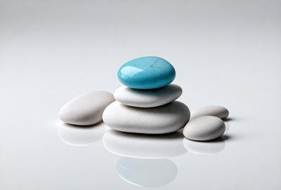 The primary subject of the image is a stack of four white rocks with a blue rock on top. The setting is a white surface, which could be a table or a wall. The visual style is a photo, capturing the natural arrangement of the rocks. The colors and mood of the image are predominantly white and neutral, giving it a clean and minimalist appearance.