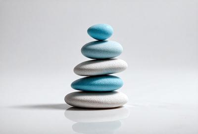 The primary subject of the image is a stack of four white and blue stones. The setting is a white background, which provides a clean and minimalist appearance. The visual style is a close-up of the stacked stones, showcasing their unique colors and textures. The overall atmosphere is calm and serene, as the stones are arranged in a simple and elegant manner.